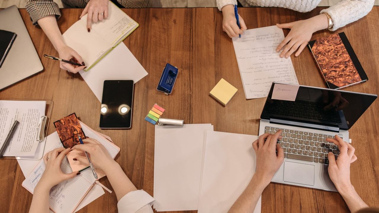 Top view of a team planning and working together in an office setting with laptops and notepads.